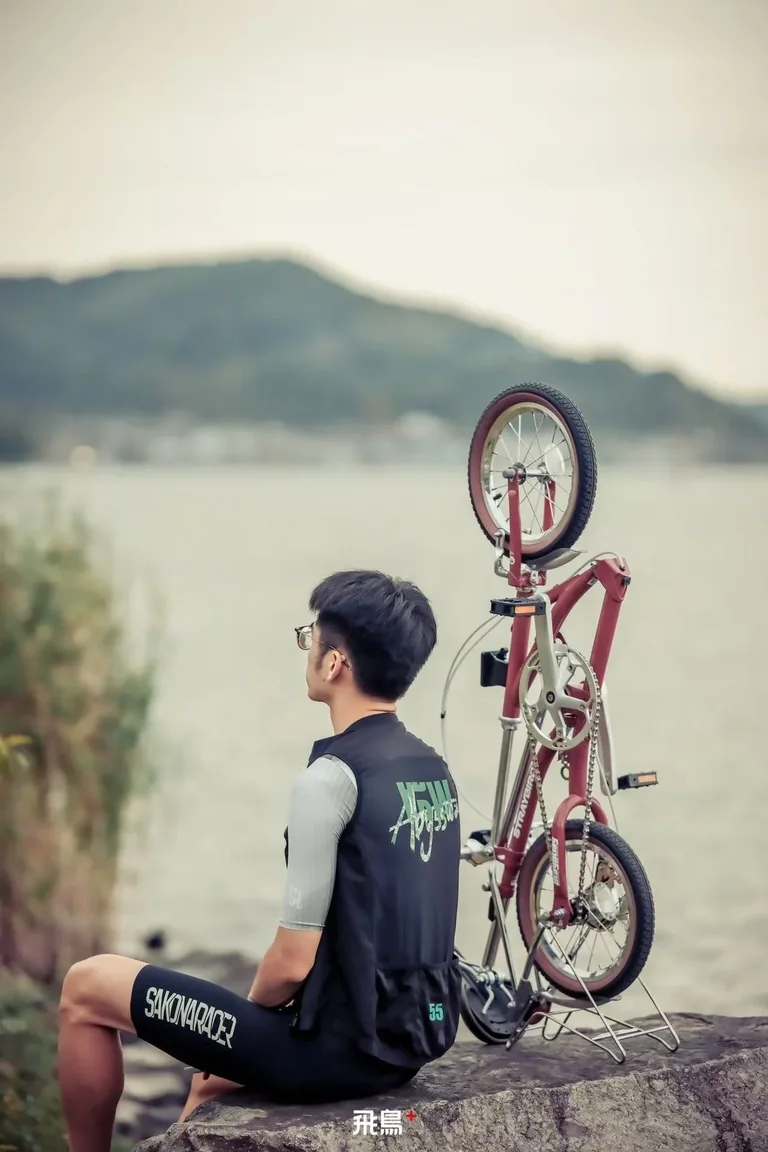 A rider sits by the lake with his folded One Touch standing beside him · 骑手坐在湖边，折好的飞鸟立在身旁